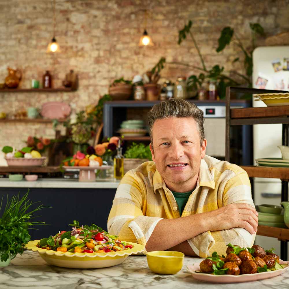 Jamie Oliver sitting at table with serving platters full of food - MyHouse