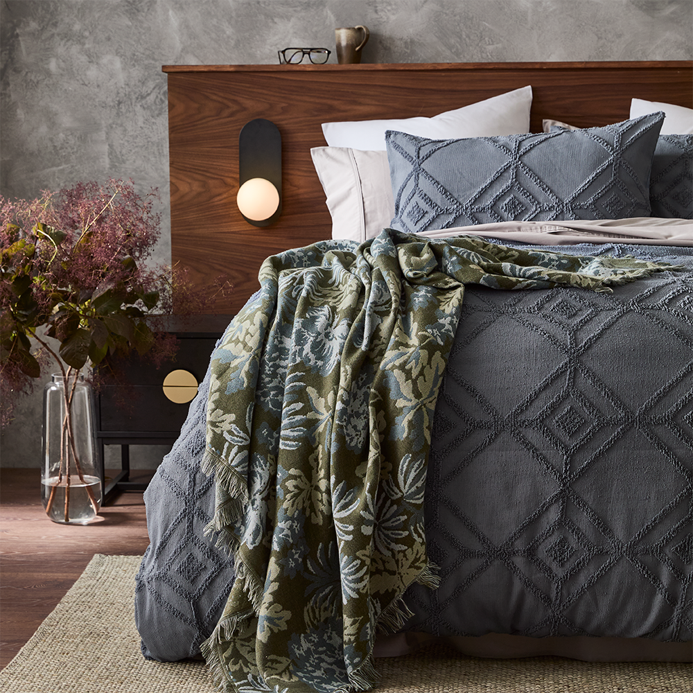MyHouse Norma throw in blue botanical tapestry design draped across a bed with decorative fringe edges