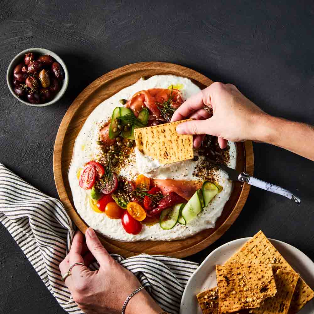 person scooping dip with corn chip from a wooden platter - MyHouse