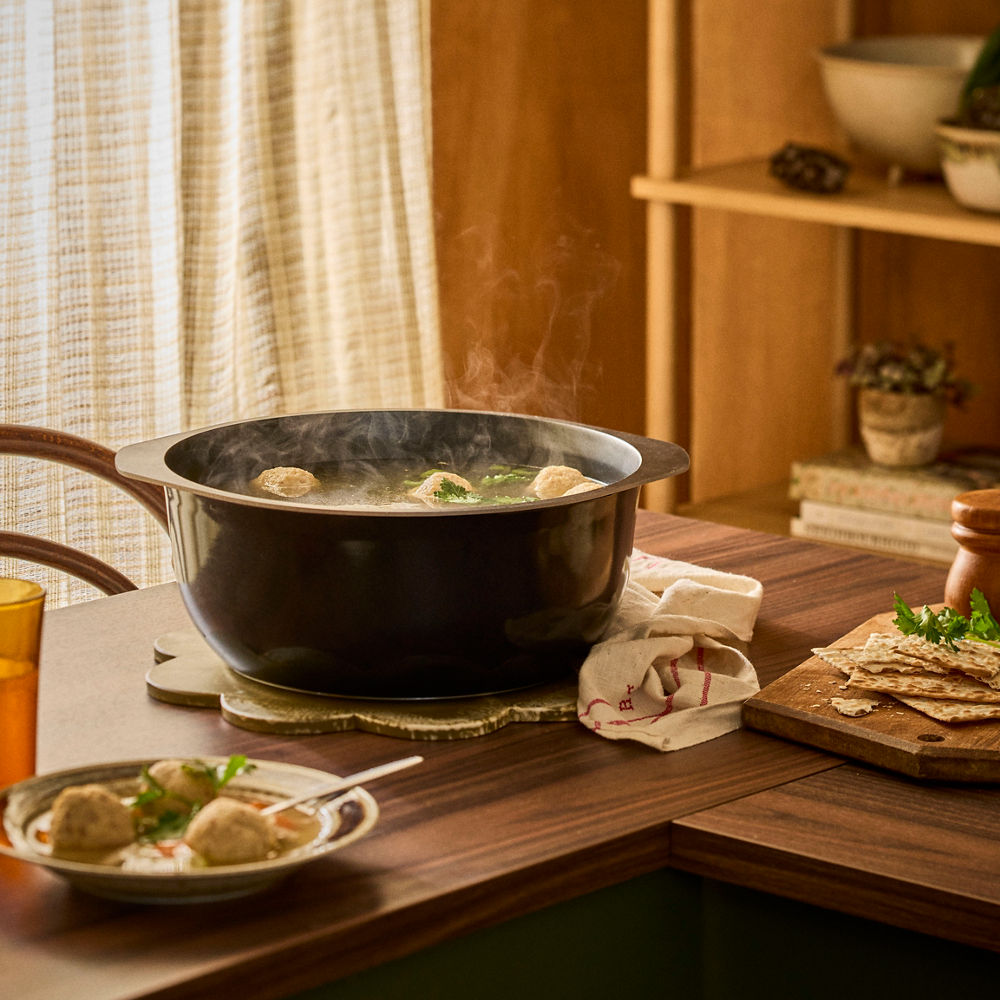 Steaming pot on a wooden table with a plate of food and a cup in the background.