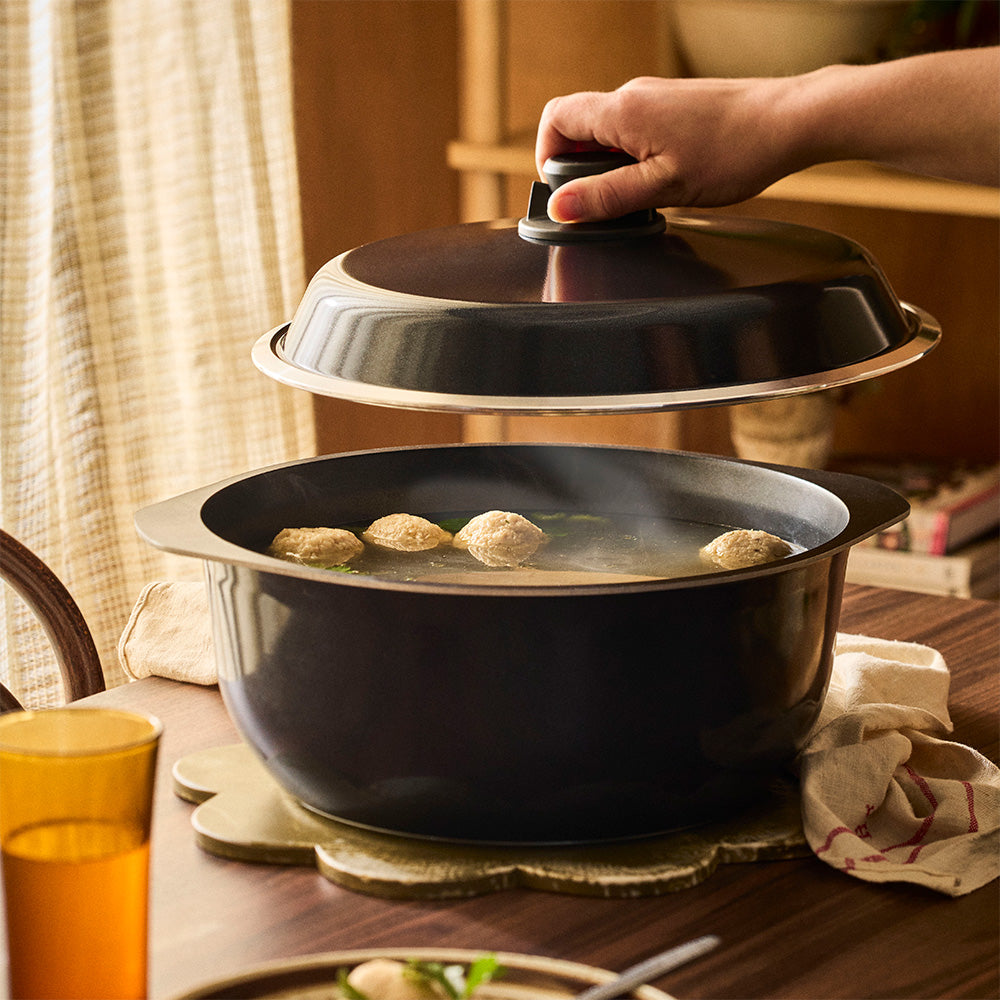 Person closing a black pot lid on a table with food inside