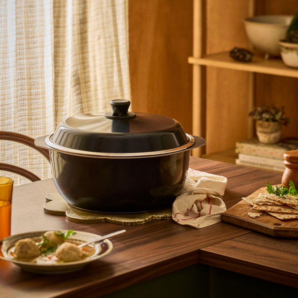 Black pot on a wooden table with food and a window in the background