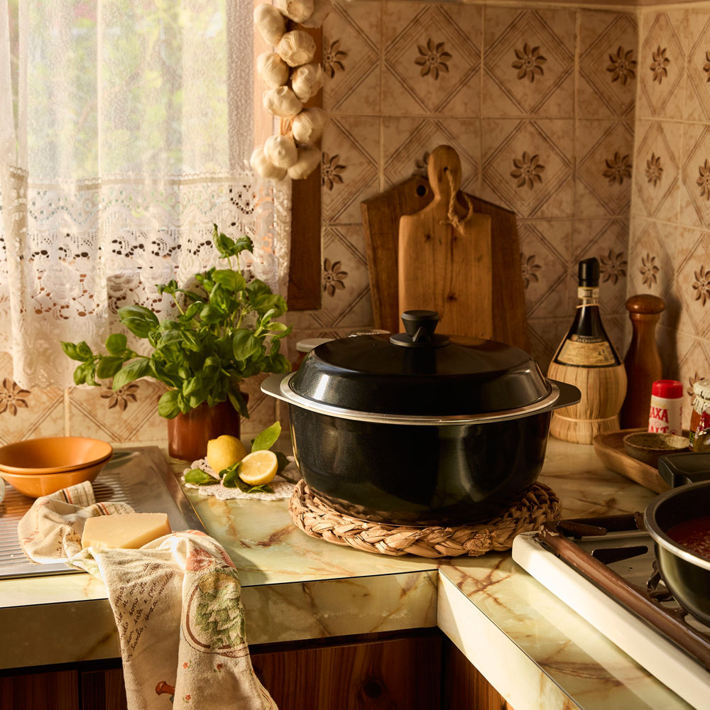 Kitchen counter with a black pot, lemons, and a plant on a tiled wall background