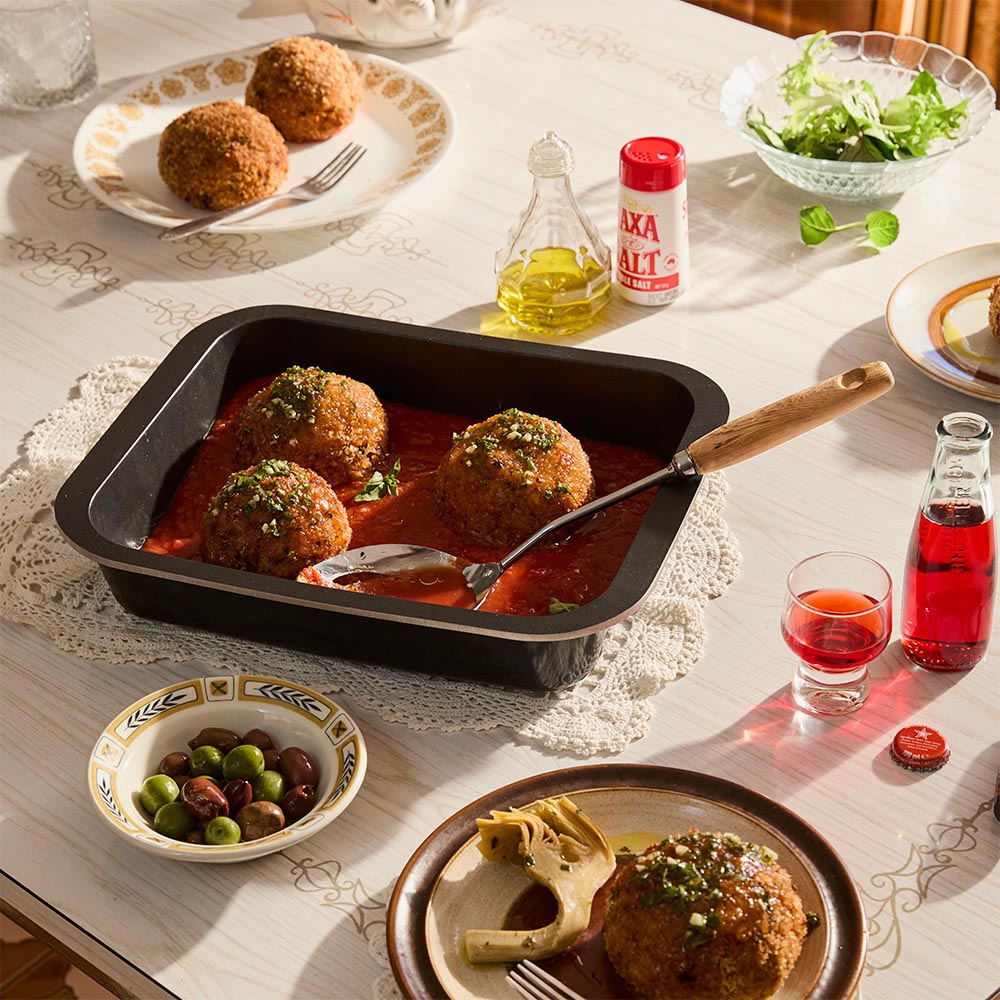 Table setting with arancini (risotto balls) in a pan, glasses of red wine, and small bowls of olives and salad.