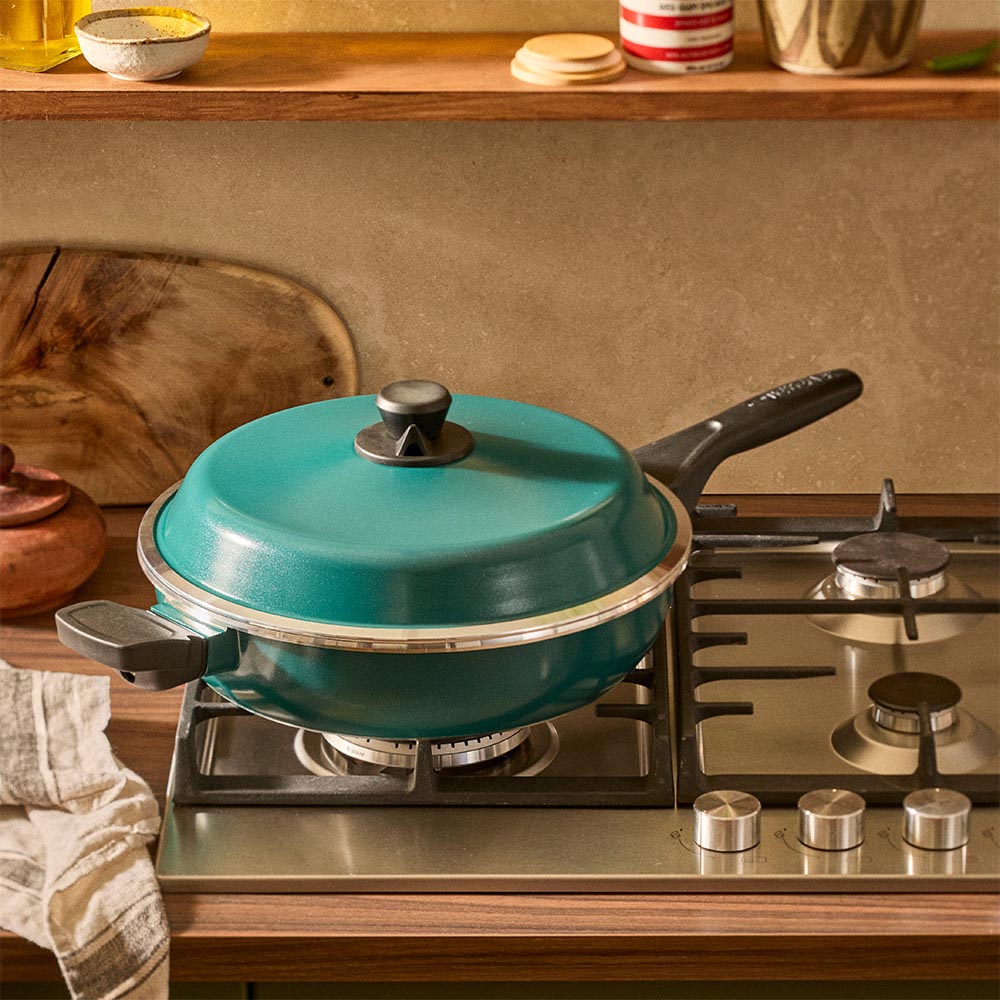 Teal frying pan with lid on a gas stove in a kitchen setting