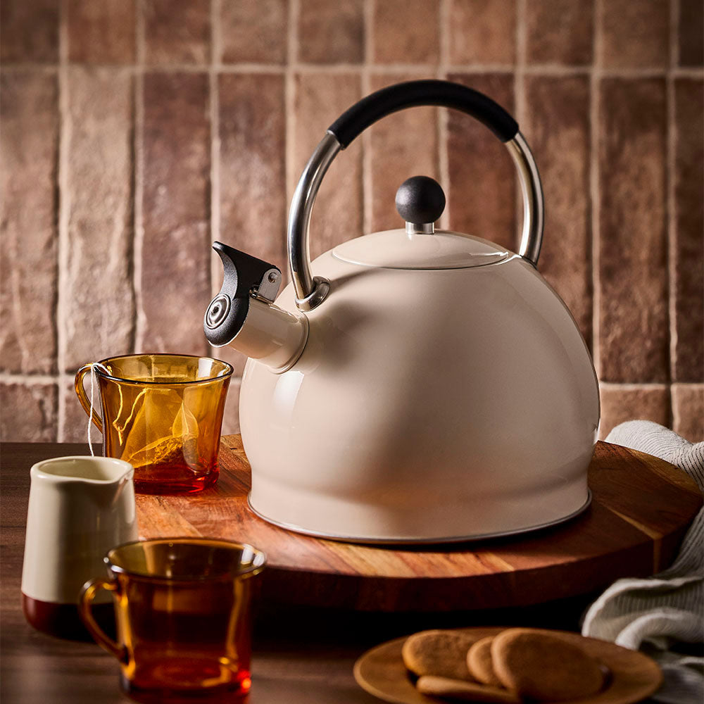 Oat stovetop kettle styled on a wooden board with an empty teacup and tea bag beside it.