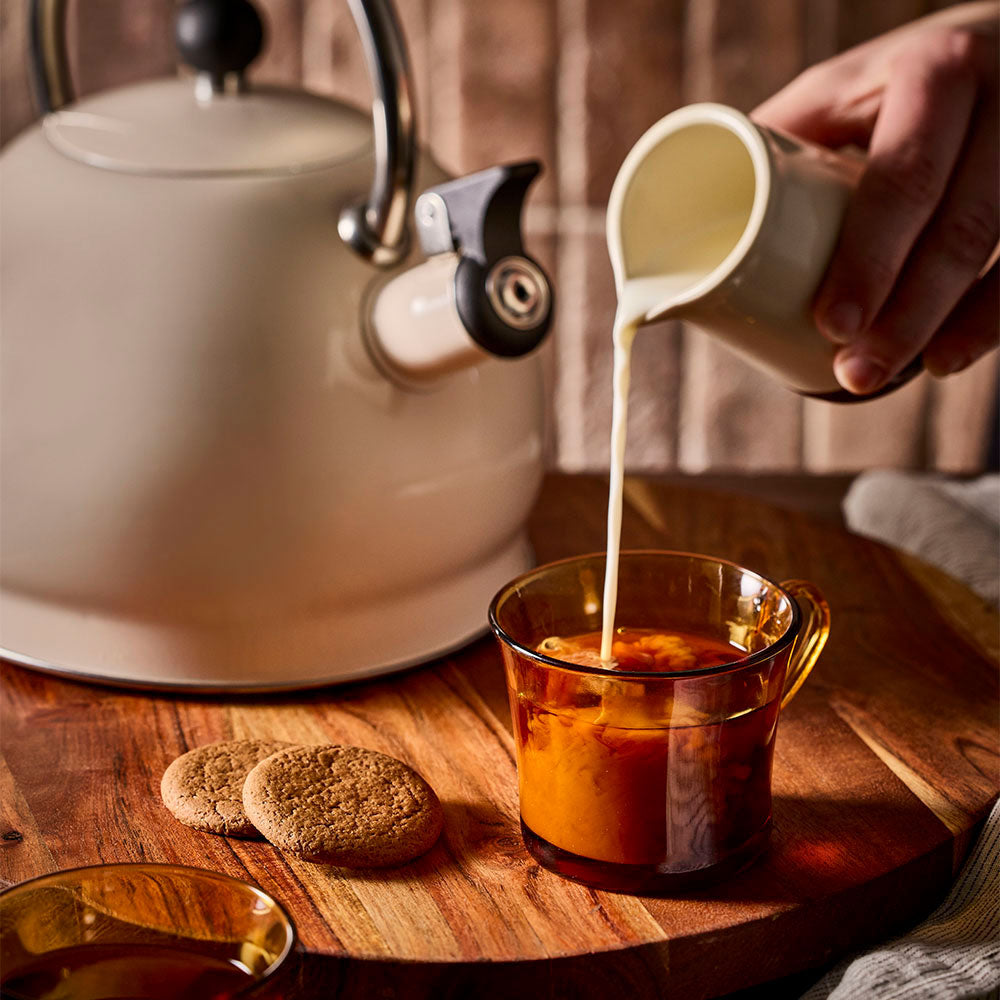 Milk being added to a cup of tea with an oat stovetop kettle positioned behind.