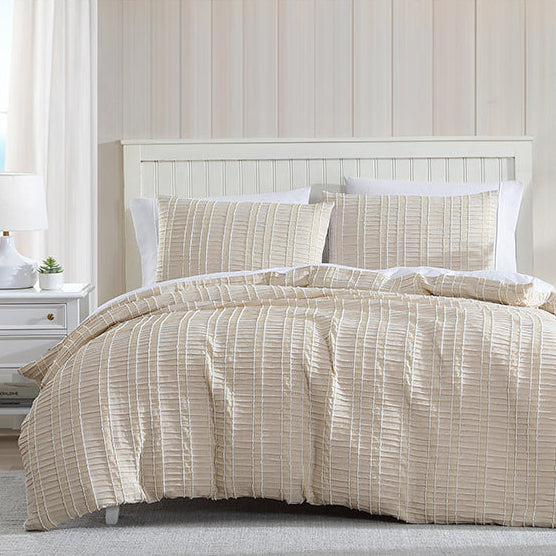 Beige striped comforter set on a bed in a bedroom with a window and shelves.
