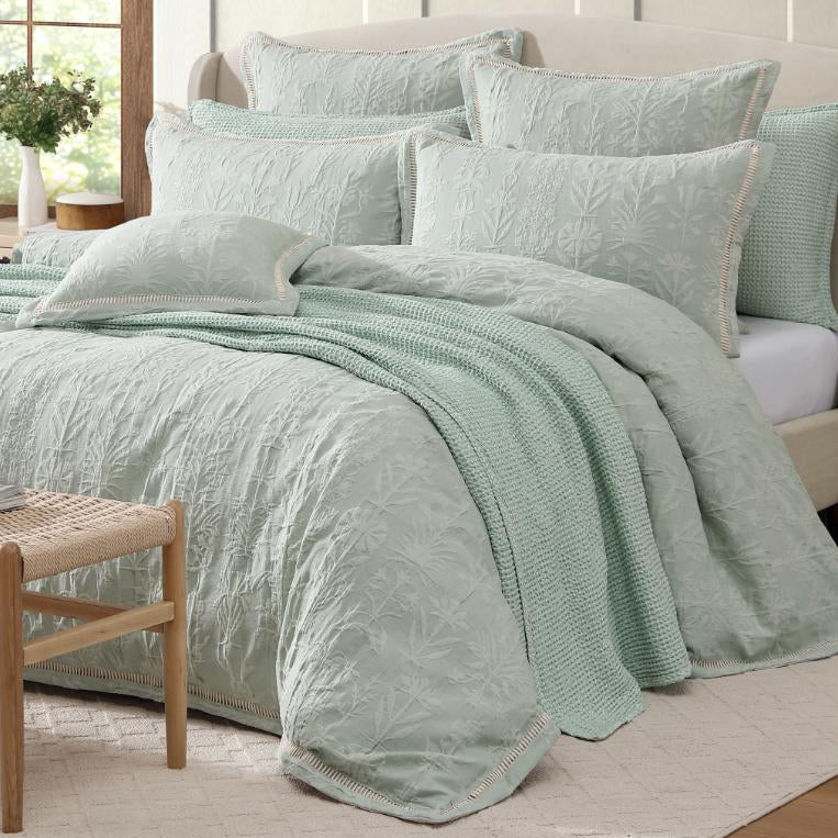 Light green textured bedding set on a bed in a bright bedroom.