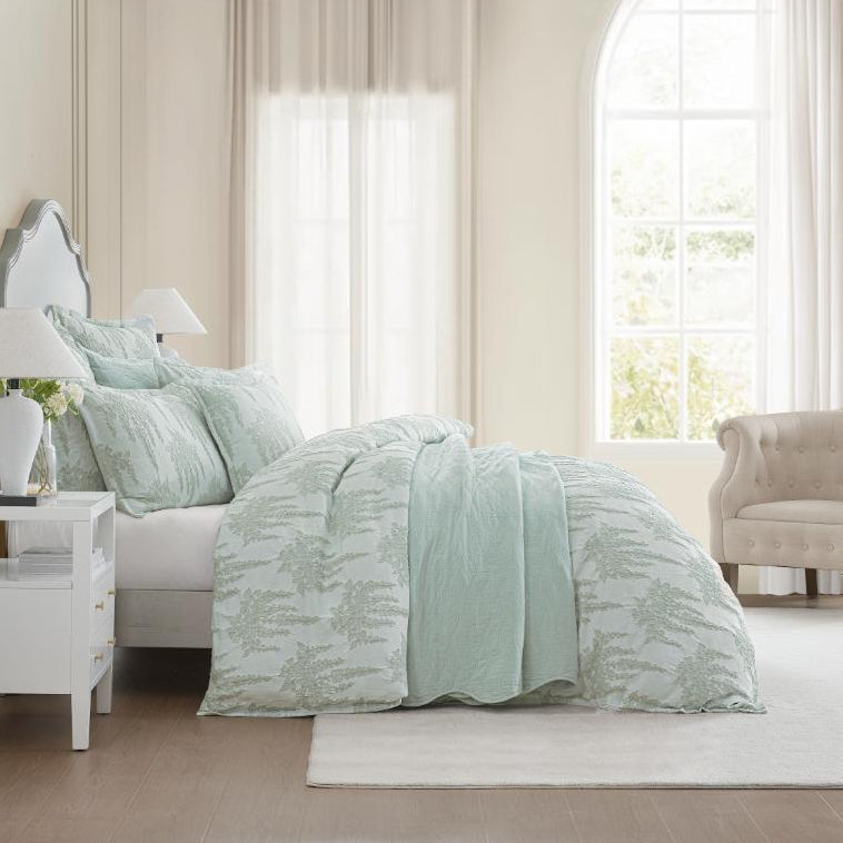 Neatly made bed with light green comforter in a bright bedroom