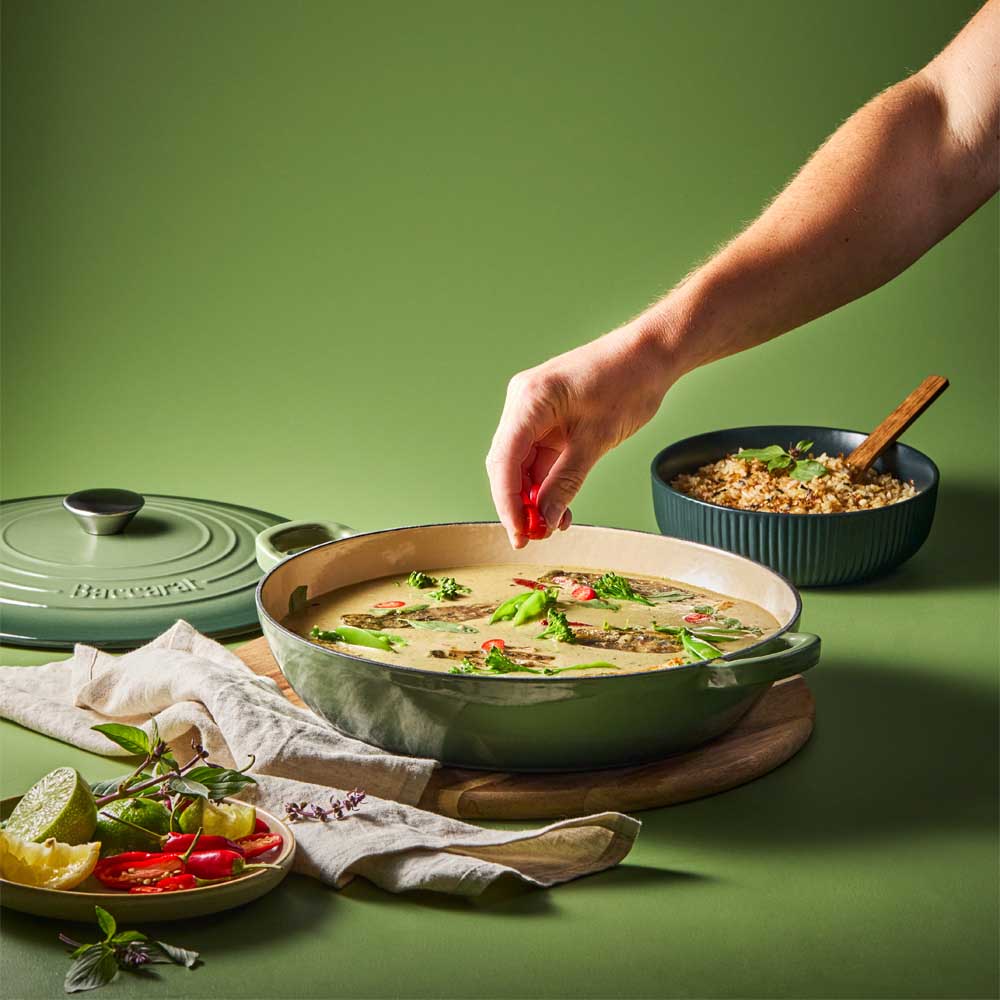 man sprinkling chilli into curry in green saute pan - MyHouse