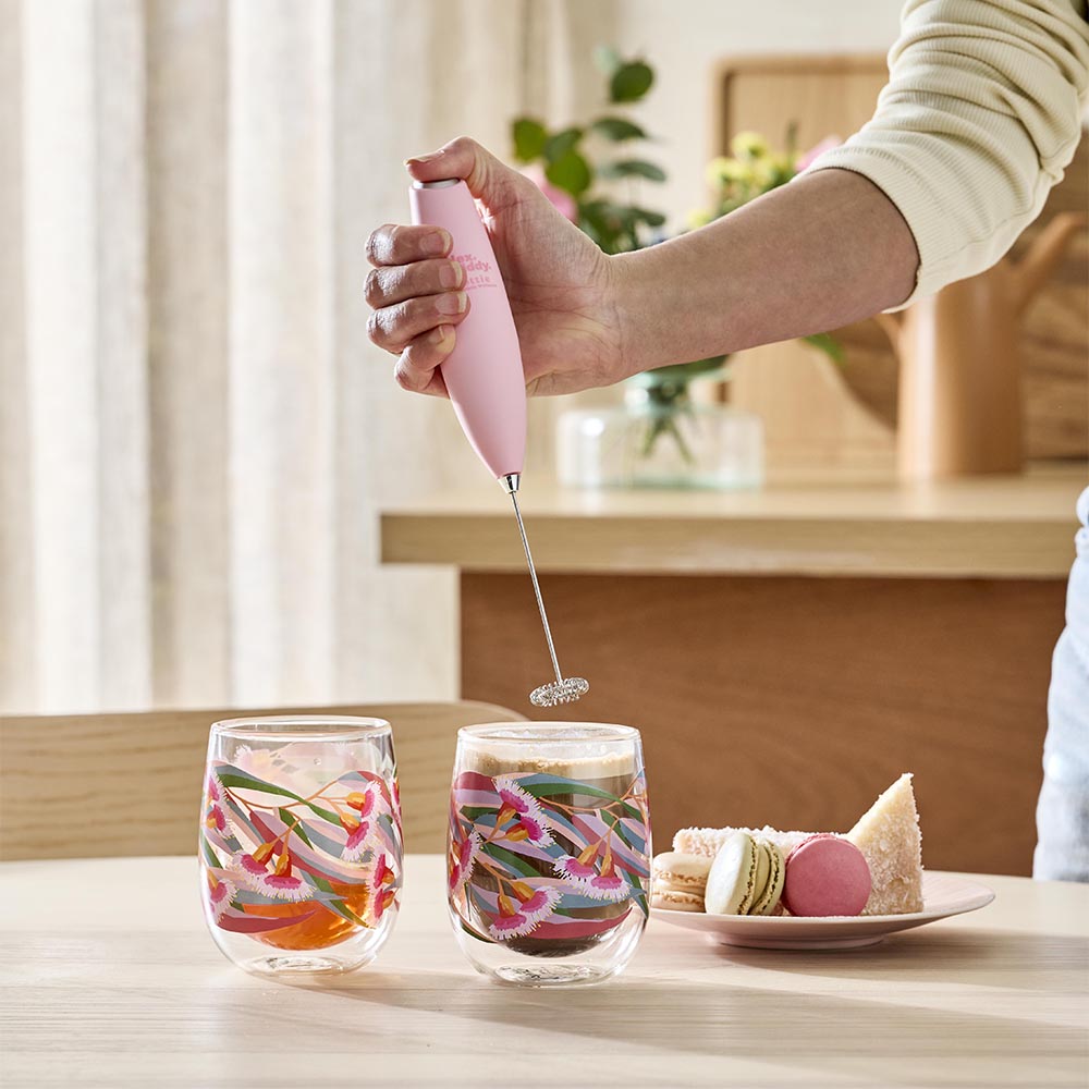 woman holding a pink milk frother above cup of coffee