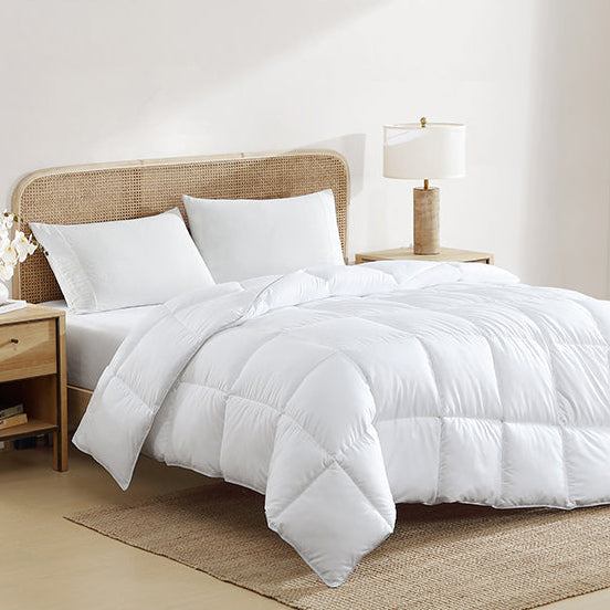 White quilt on a bed in a bright bedroom with wooden furniture.