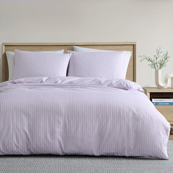 Bed with purple bedding in a room with wooden furniture and decor.